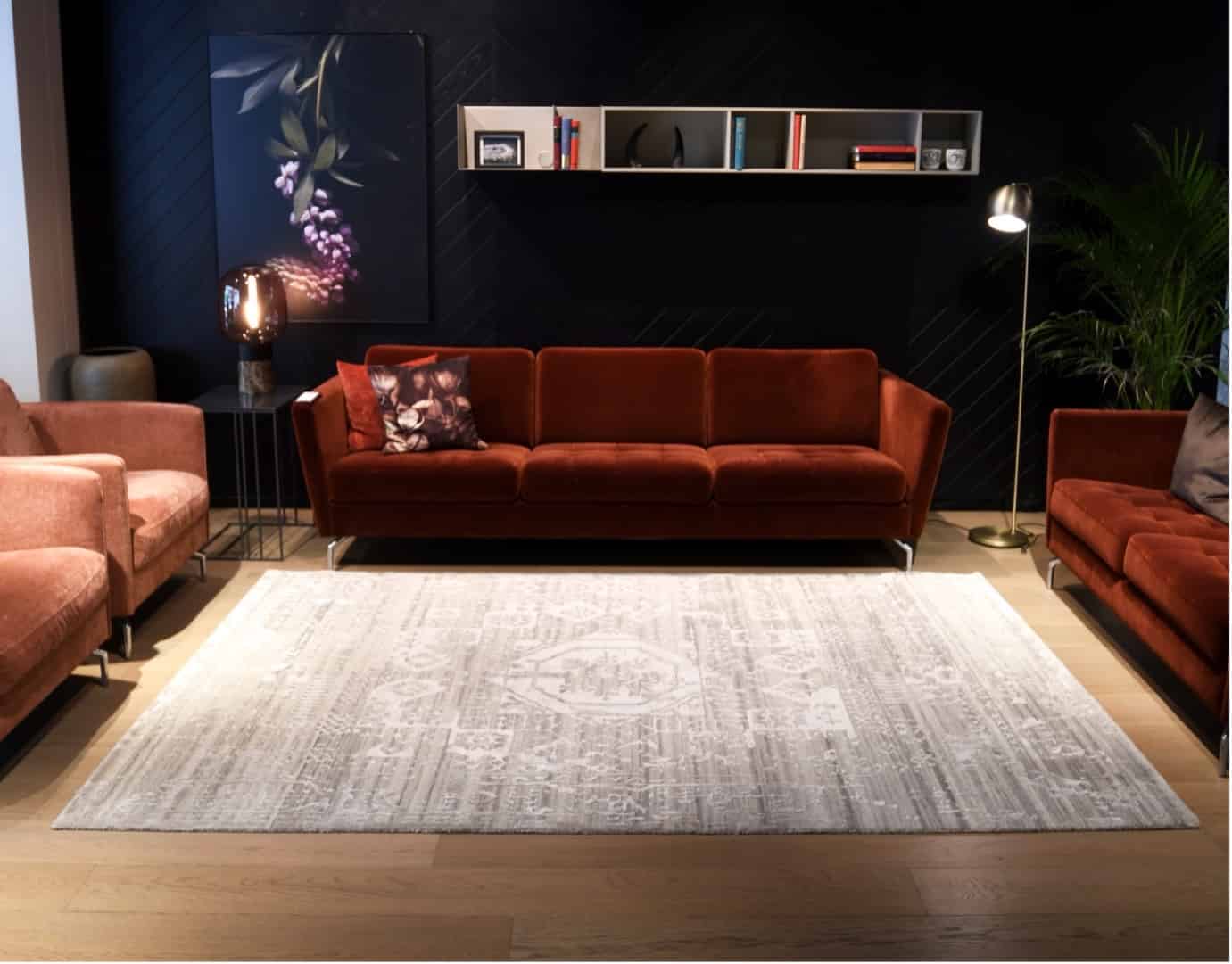 Beige carpet with intricate designs by Carpet Cellar on a wooden floor, surrounded by red sofas