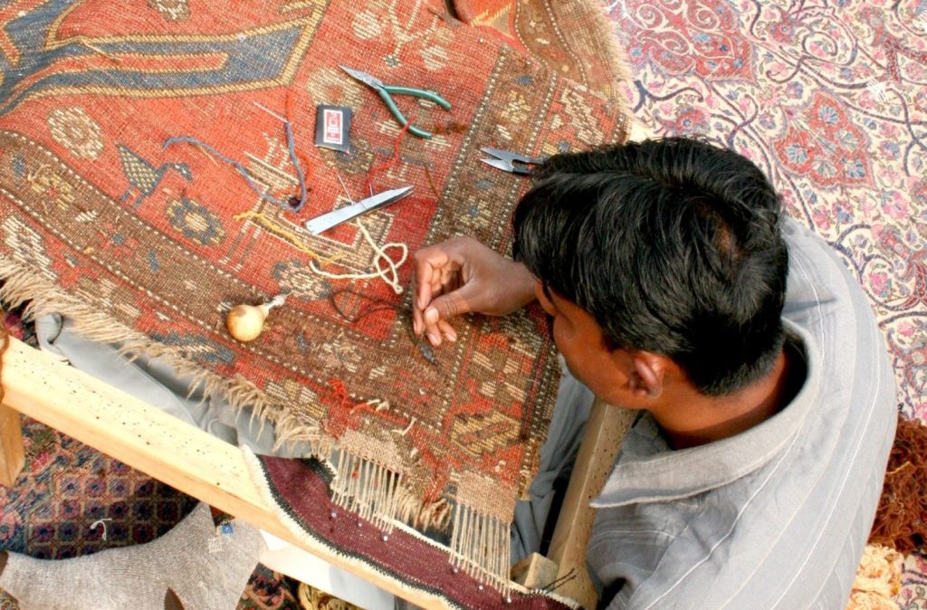 Artisan restoring a rug with recycled fibers at Carpet Cellar